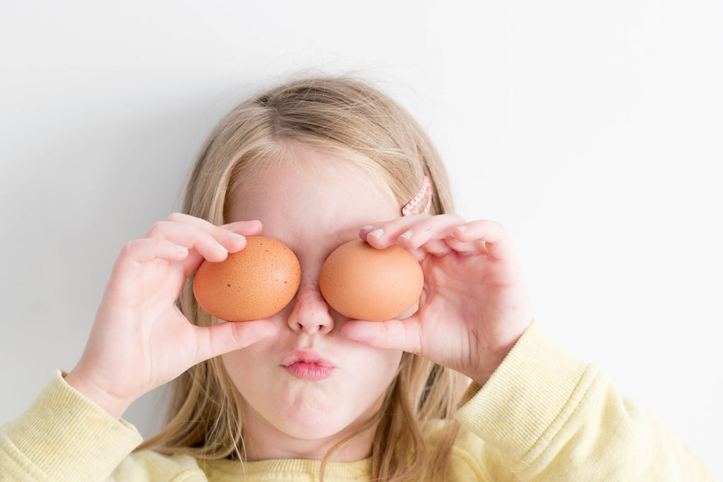 child holding up two eggs in from of their eyes and pouting